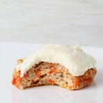 one frosted carrot cake cookie with a bite taken on a white background.