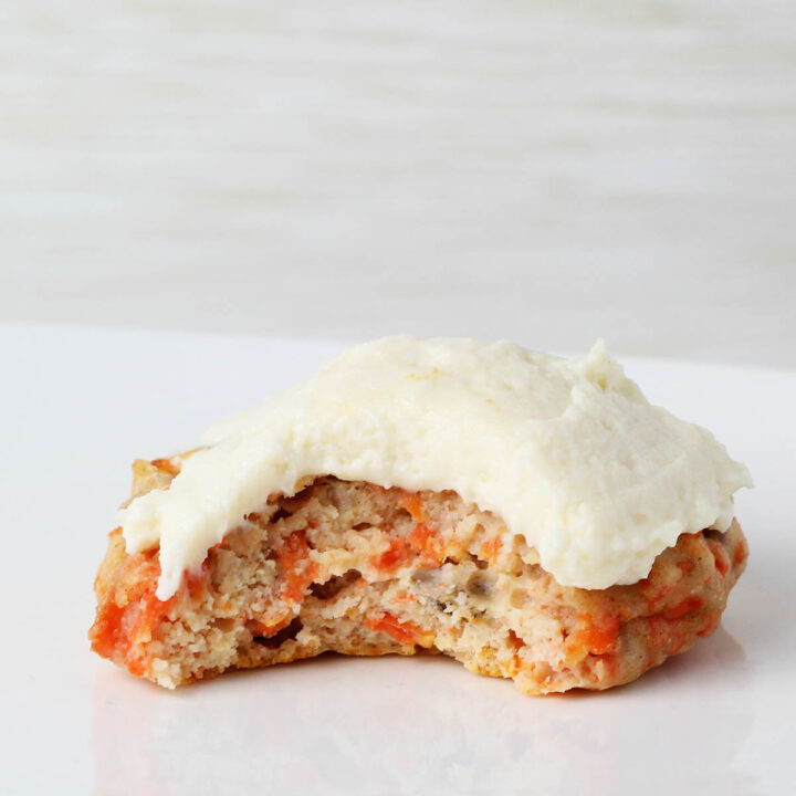 one frosted carrot cake cookie with a bite taken on a white background