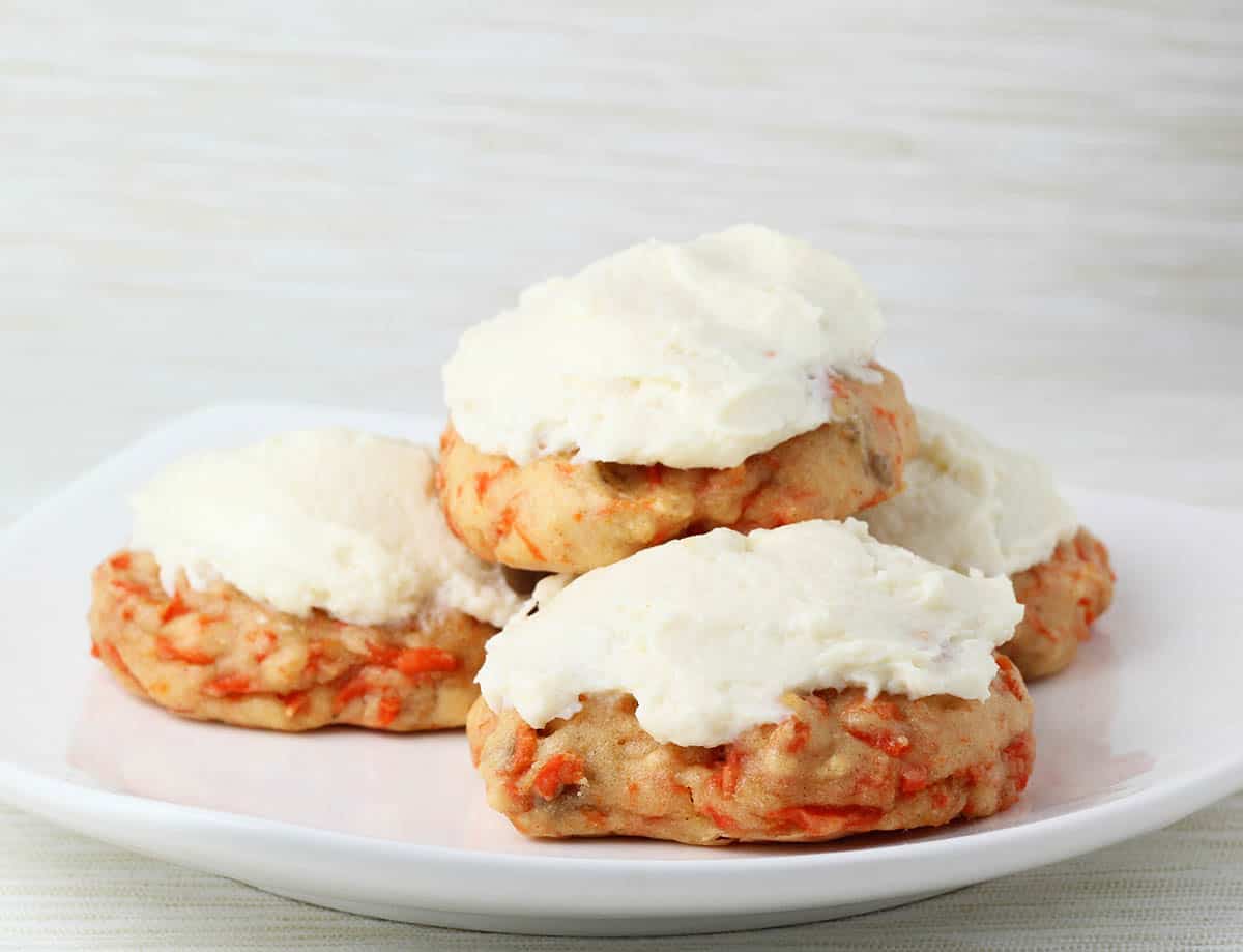 a pile of frosted carrot cake cookies on a white background.