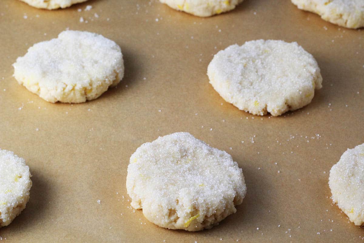 unbaked lemon cookies topped with erythritol on a sheet of unbleached parchment paper