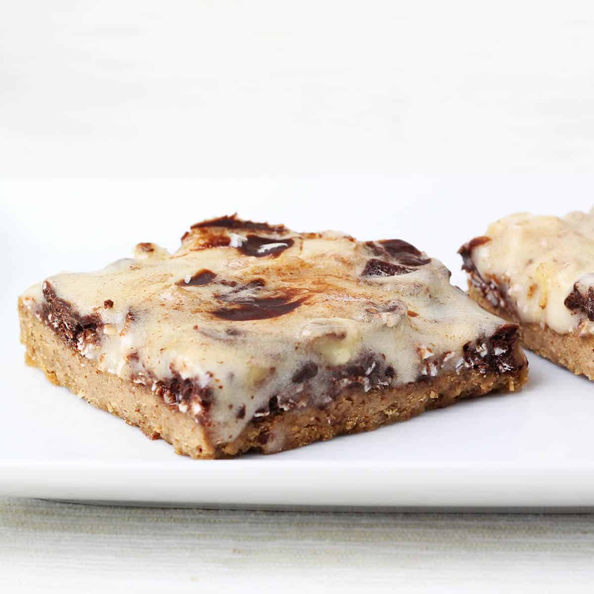 angled front view of a healthy magic bar with cookie layer and topped with chocolate, coconut, and whey icing layer