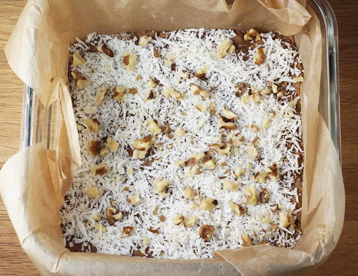 coconut walnut layer of healthy magic bars in a square glass baking dish lined with unbleached parchment paper