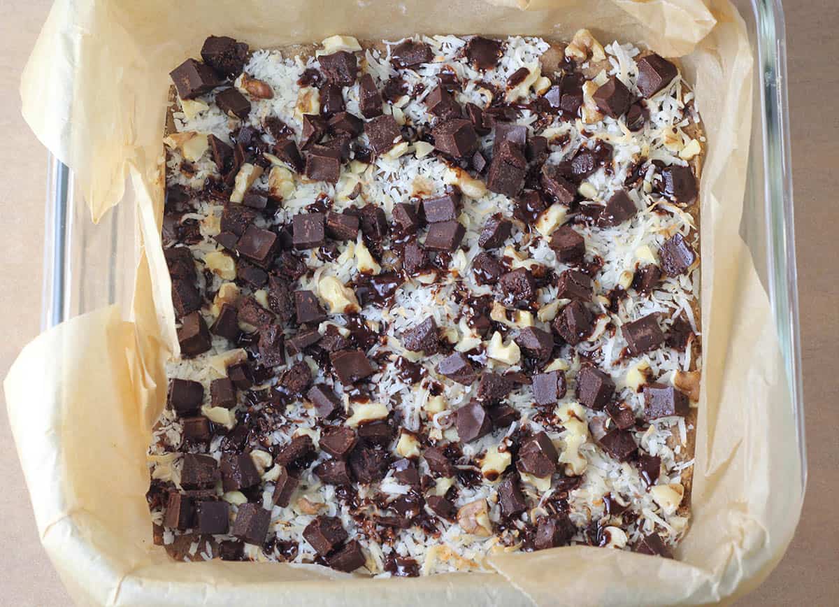 chocolate chunk layer of healthy magic bars in a square glass baking dish lined with unbleached parchment paper
