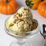 pumpkin ice cream with chunks of protein pie crust ina serving dish with mini pumpkins in the background