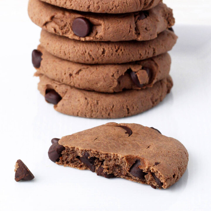 stack of healthy vegan double chocolate chip cookies with one half cookie in front on a white background
