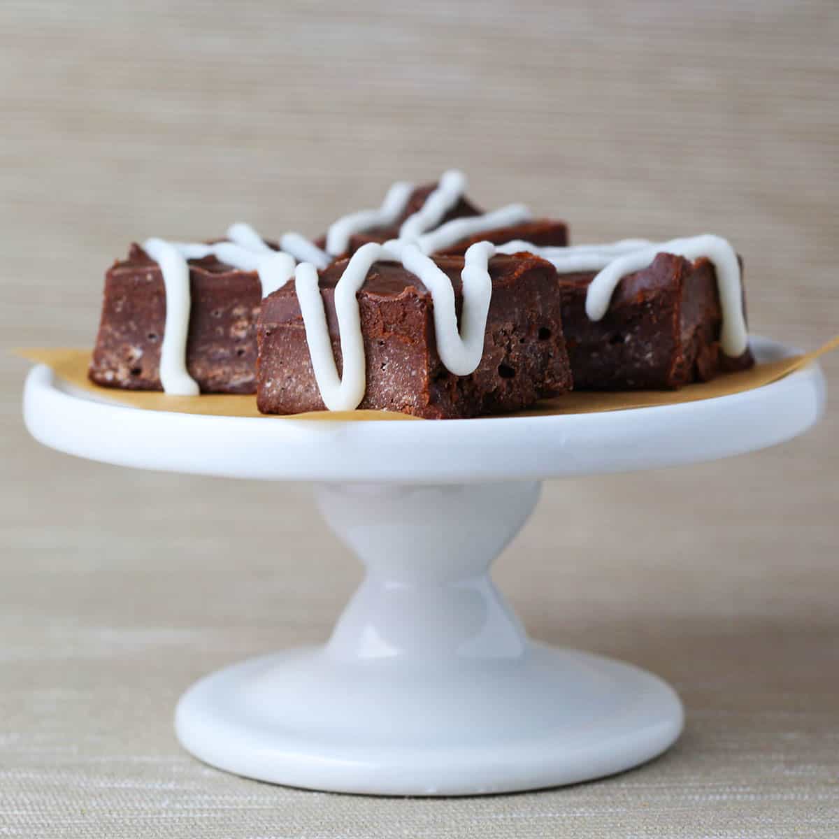 iced pieces of keto fudge on a cupcake stand with a beige background