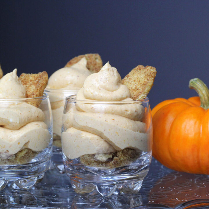 straight on view of pumpkin cheesecake mousse in shot glasses with a mini pumpkin on an etched glass cake stand