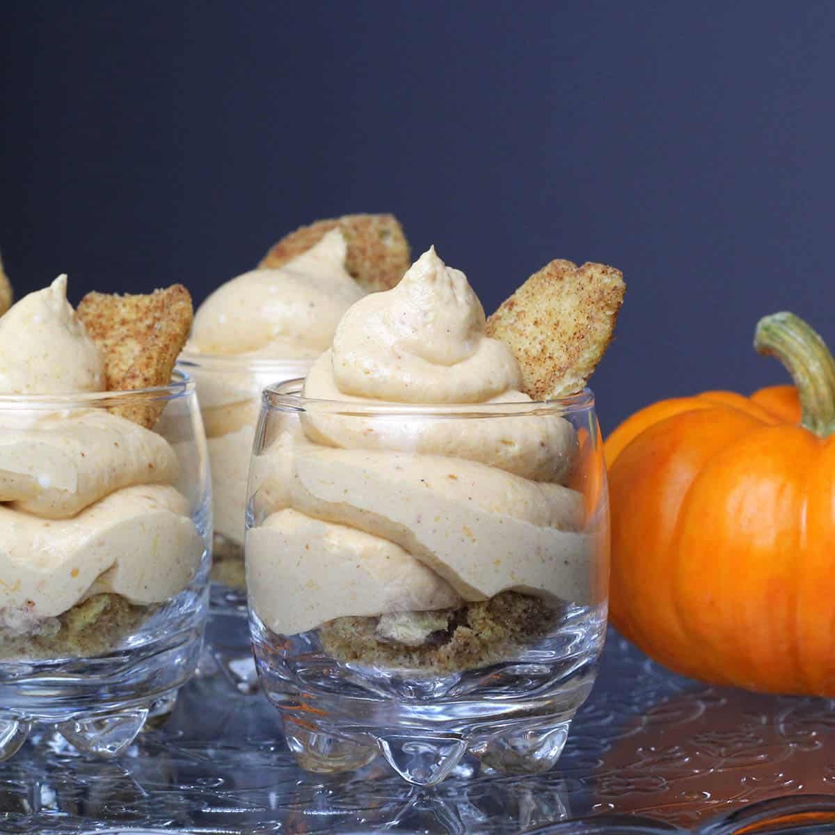straight on view of pumpkin cheesecake mousse in shot glasses with a mini pumpkin on an etched glass cake stand