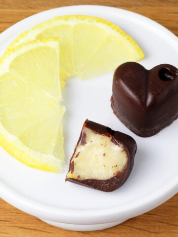 round serving plate with two slices of lemon and two heart-shaped filled chocolates, one open with the filling showing