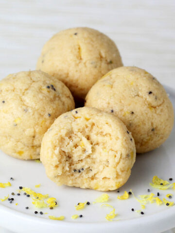 three full and one bitten lemon poppy seed protein ball on a white cupcake stand with lemon zest and poppy seeds and with a light background