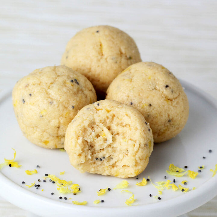 three full and one bitten lemon poppy seed protein ball on a white cupcake stand with lemon zest and poppy seeds and with a light background