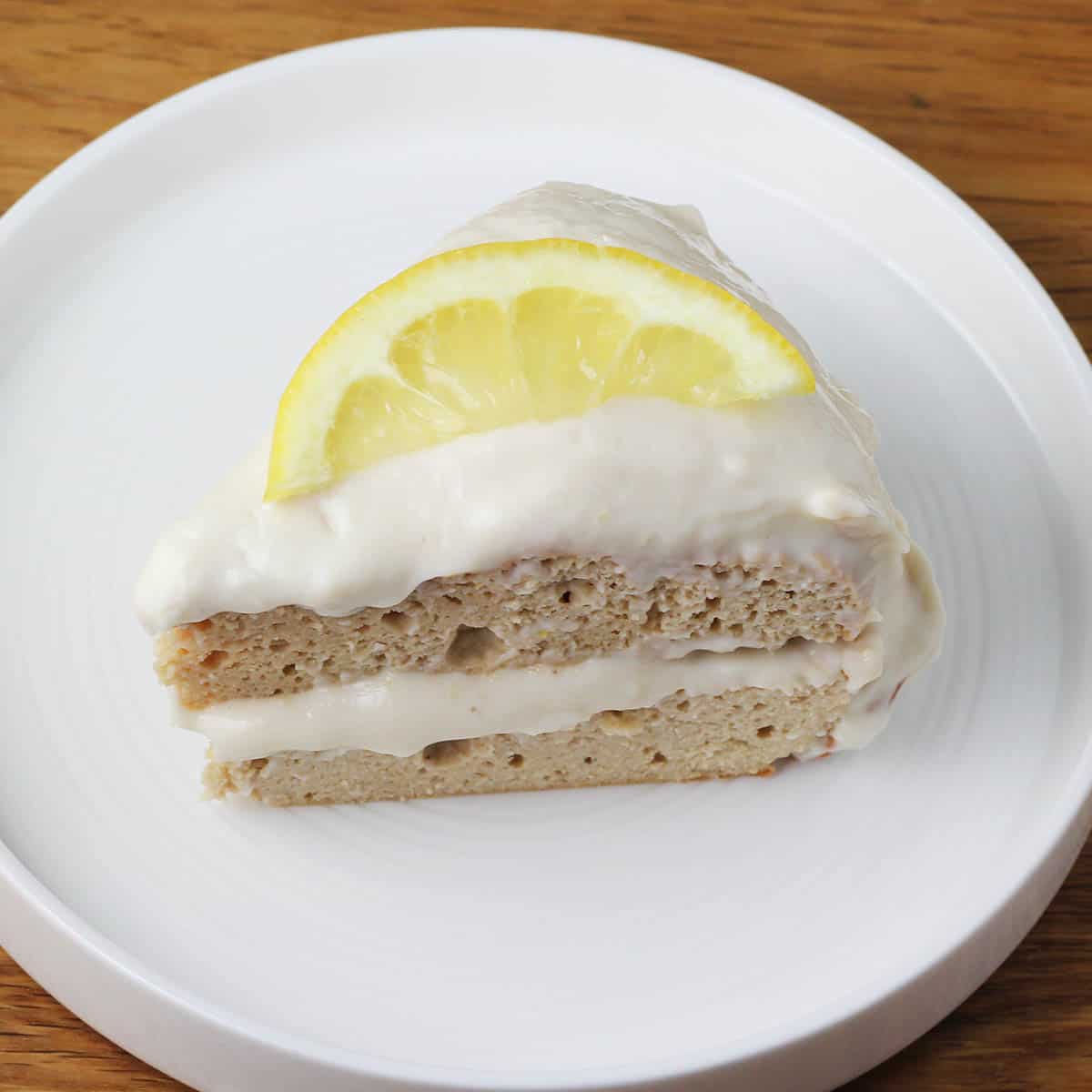 slice of lemon protein layer cake topped with yogurt frosting and a slice of lemon