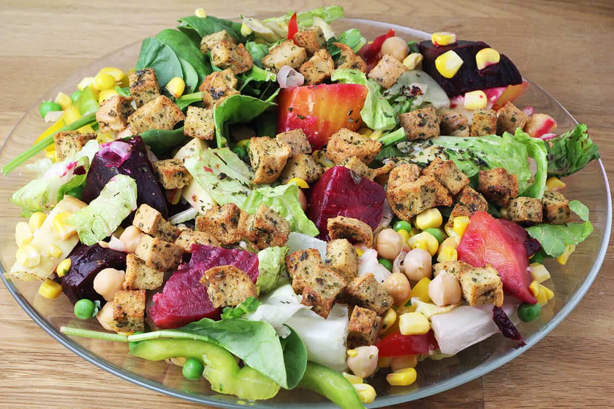 a bright and colorful slald with beets, corn, cucumber, spinach, chickpeas, and low carb homemade croutons