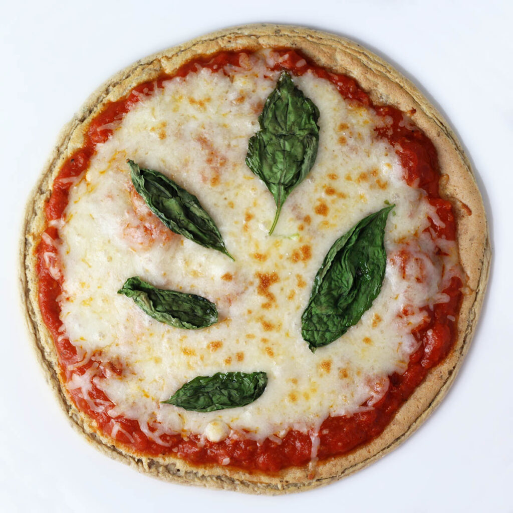 overhead view of low carb gluten free pizza topped with basil leaves on a white background