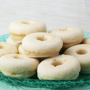 several glazed mini donuts on a green glass plate with a light backgroud
