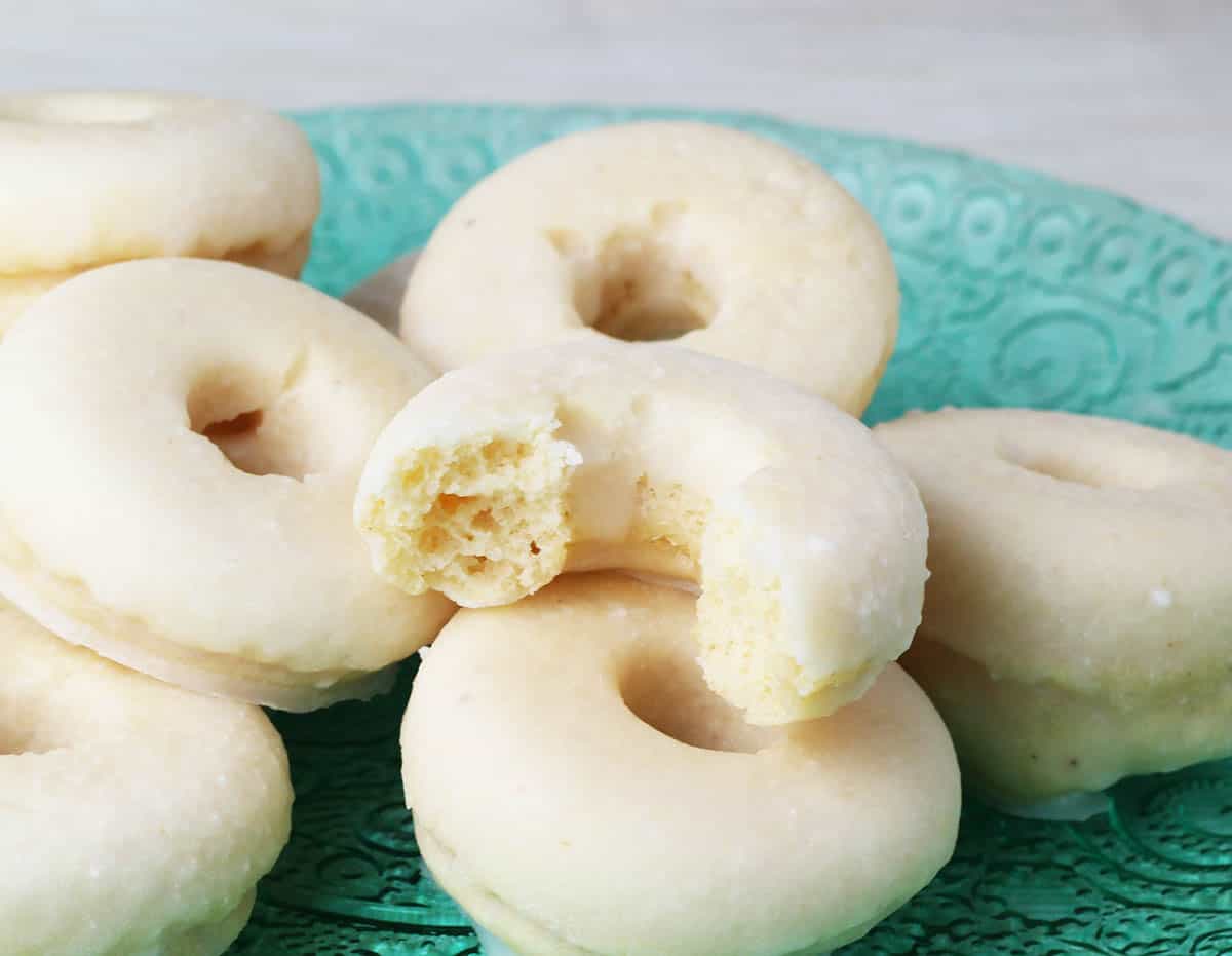 several glazed mini donuts with one bitten on a green glass plate