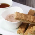 pancake sticks on a white plate with one dipped in cinnamon erythritol and next to maple syrup