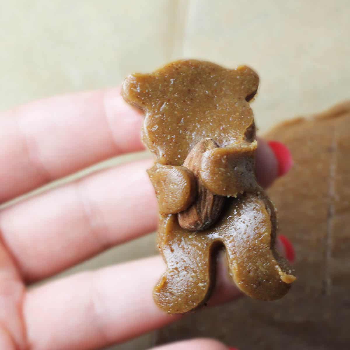 an unbaked bear cookie hugging an almond in a woman's hand
