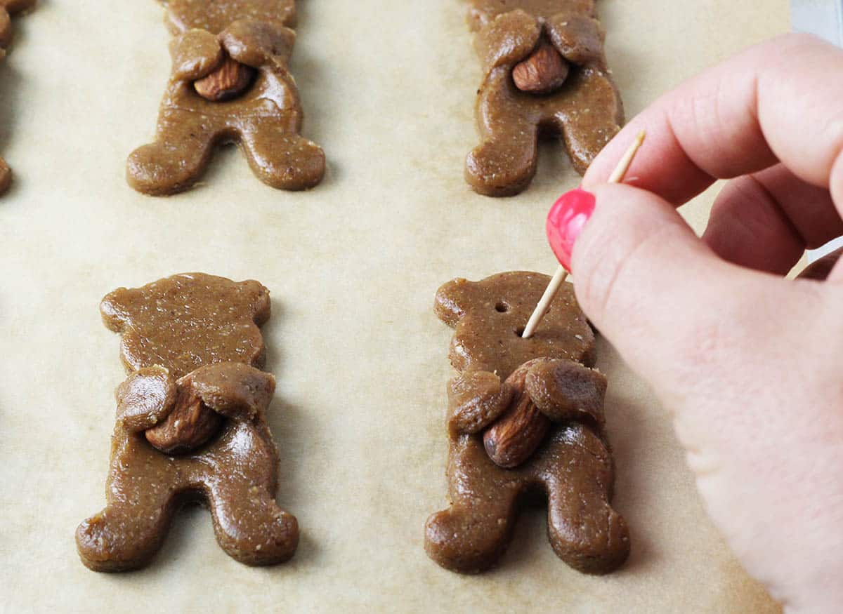 unbaked bear hug cookies on parchment paper with a woman's hand poking holes for eyes and nose with a toothpick