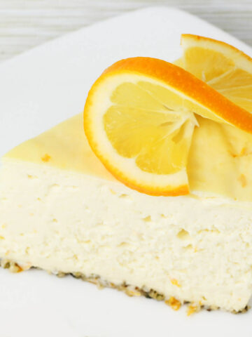 slice of cheesecake with hemp heart crust and a twisted slice of meyer lemon on top, on a white plate