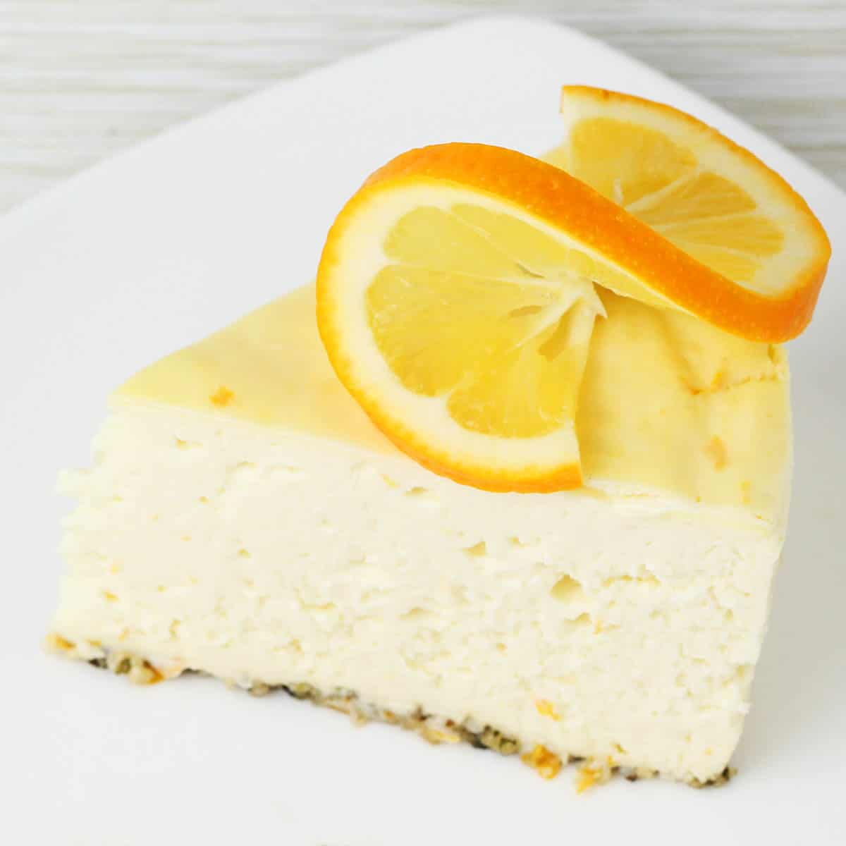 slice of cheesecake with hemp heart crust and a twisted slice of meyer lemon on top, on a white plate