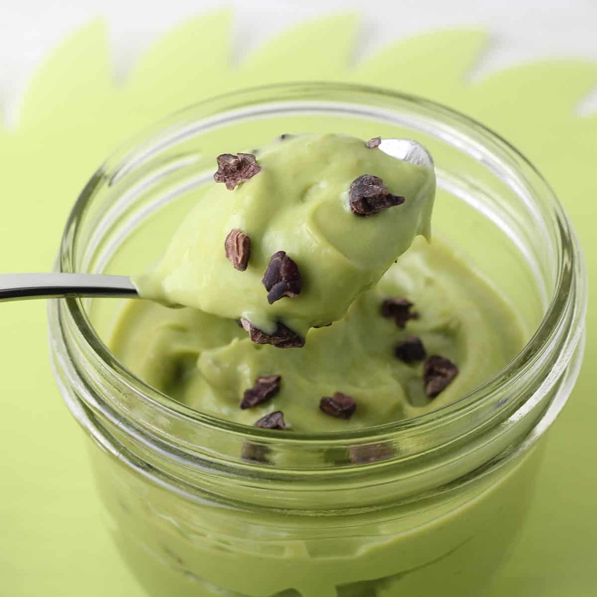 small jar with green mint mousse and cacao nibs with a mint green background