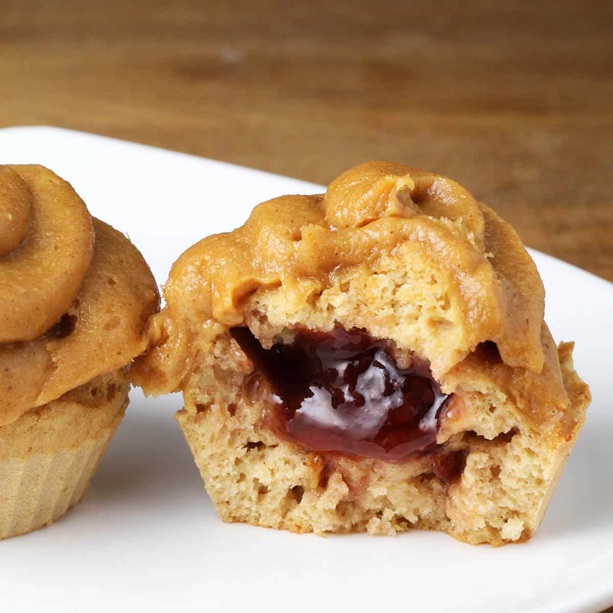 inside view of a peanut butter and jelly cupcake, which is a peanut butter cupcake filled with jelly and topped with peanut butter protein frosting on a white plate on a wood table