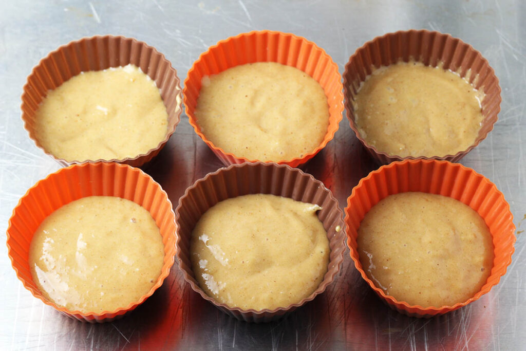 six silicone cupcake cups with peanut butter protein cake batter in them, the cups are orange and brown alternating colors