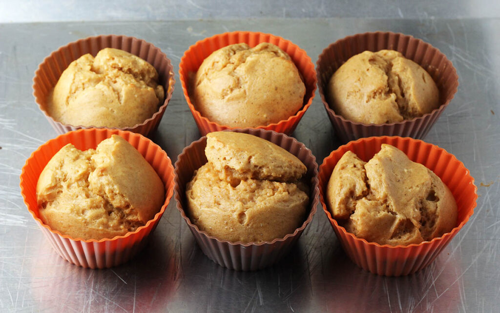 six silicone cupcake cups with baked peanut butter protein cake in them, the cups are orange and brown alternating colors