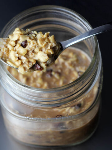 top view of a small mason jar with overnight oats in it and a spoonful on top with a dark background and lit from the left