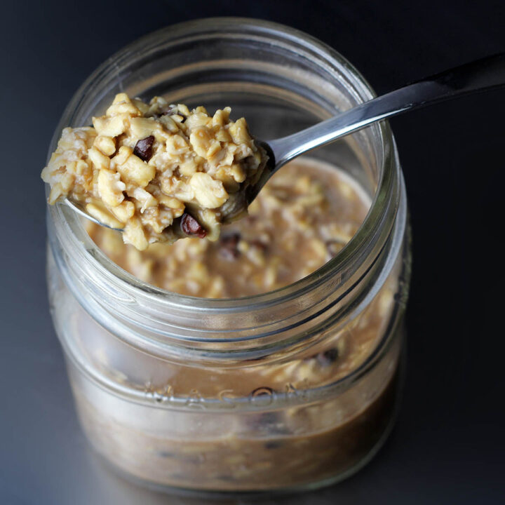 top view of a small mason jar with overnight oats in it and a spoonful on top with a dark background and lit from the left