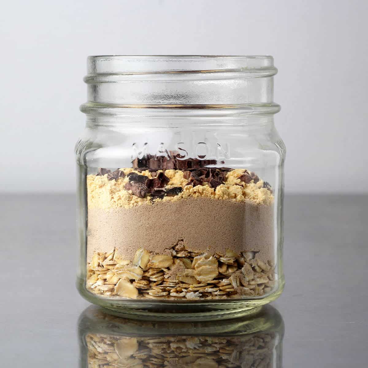 a small mason jar with layered dry ingredients of oats, chocolate protein powder, powdered peanut butter and cacao nibs