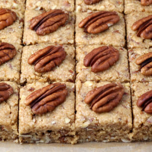 close up of freshly cut pecan protein squares, each topped with a pecan half