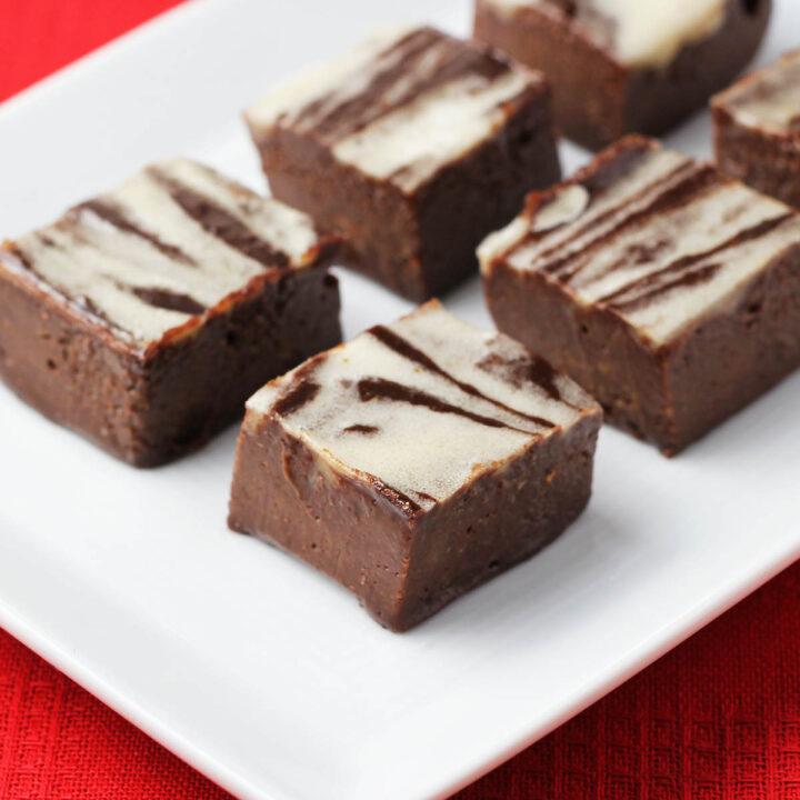 chocolate fudge with white peppermint swirls on a white plate on a red linen.