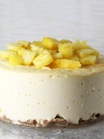 front view of a pineapple topped protein cheesecake on a flower etched glass cake plate with a light background