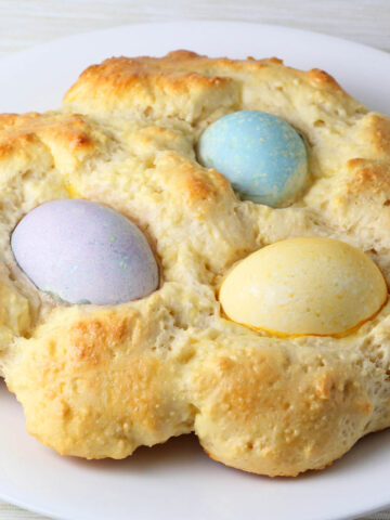 rounded loaf of protein bread with three colored easter eggs baked into it, the eggs are colored purple, blue, and yellow