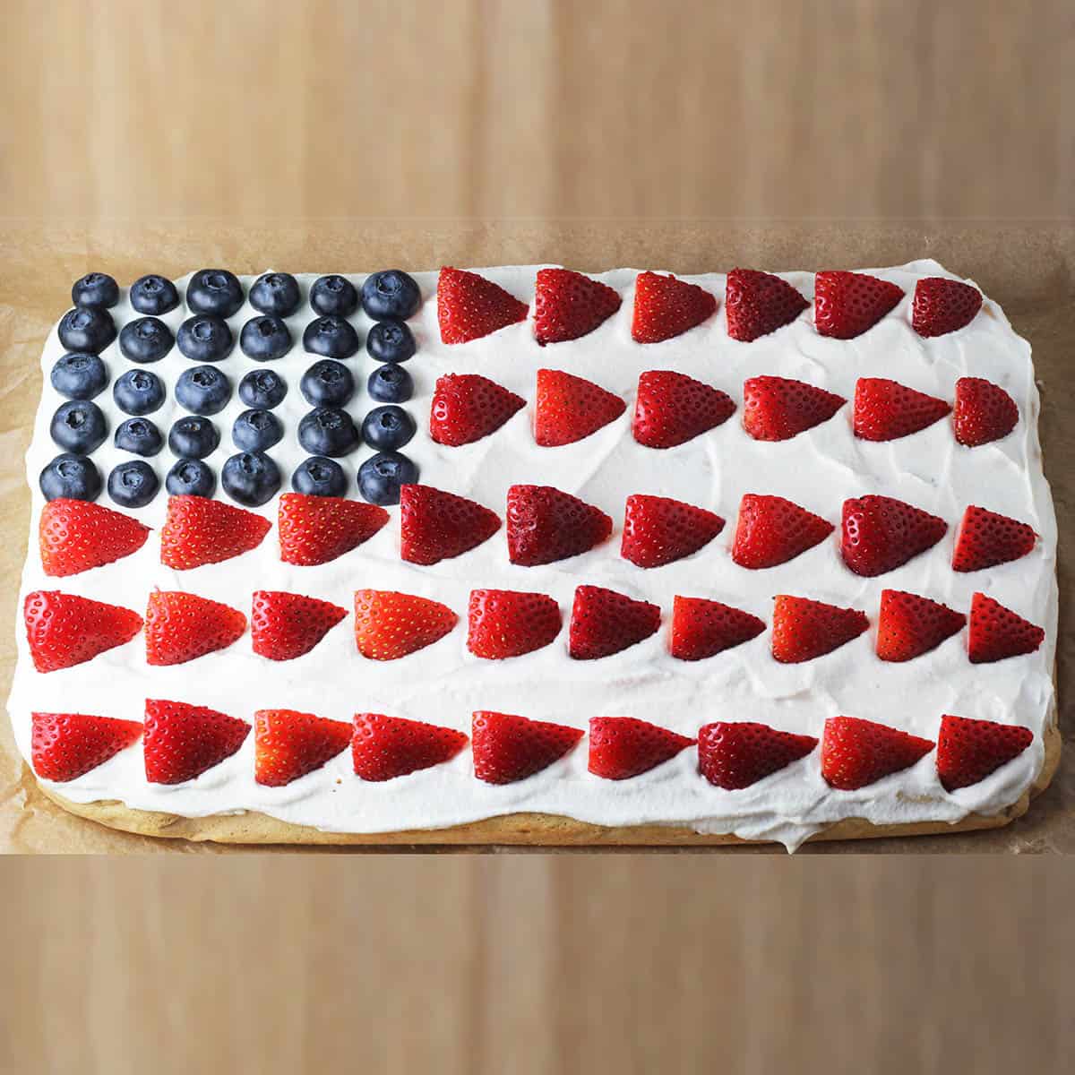 flag cake - vanilla sheet cake with whipped cream frosting with blueberries and sliced strawberries places to represent the American flag