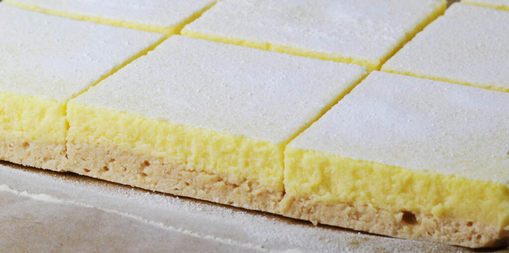 freshly cut protein lemon bars on a sheet of parchment paper with confectioners erythritol dusting on top