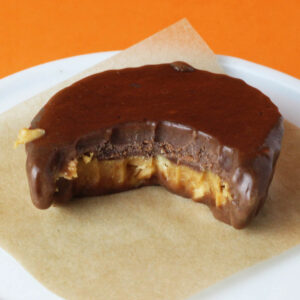 one bitten chocolate peanut butter fudge cup on a white plate with orange background