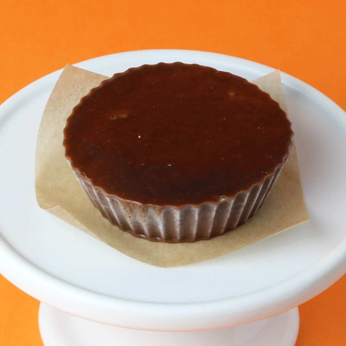 one chocolate peanut butter fudge cup on a white plate with orange background