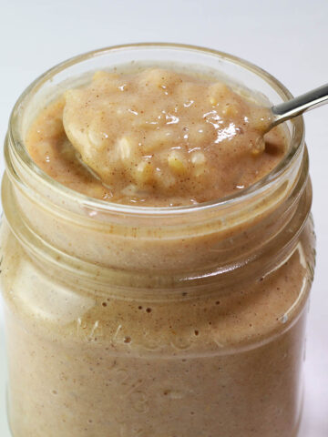 small mason jar full of rice pudding with a spoon pulling some out of the top with a light background