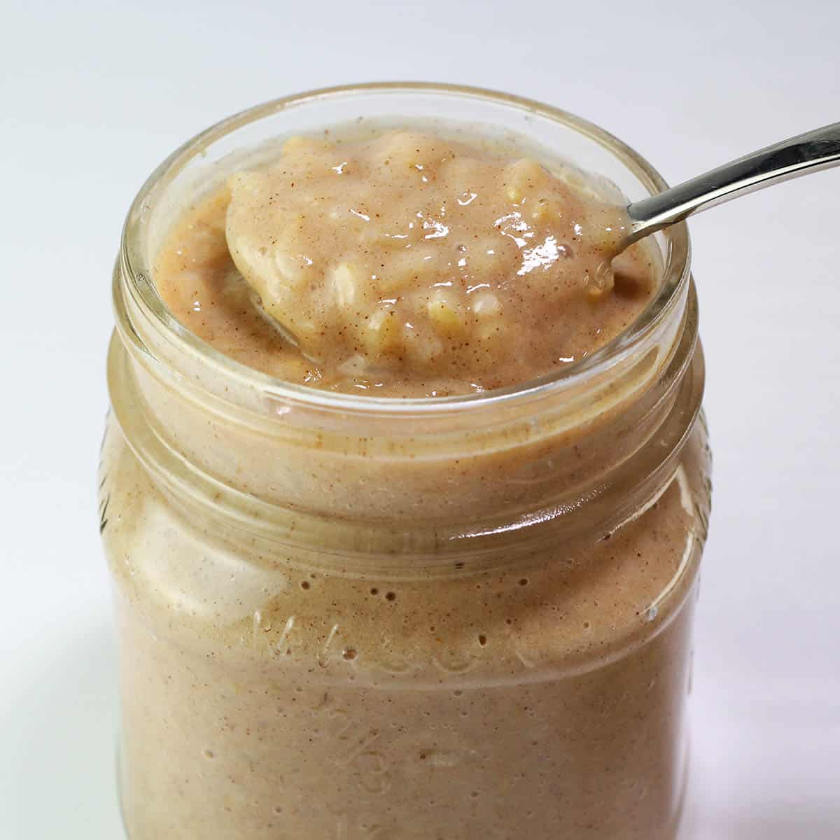 small mason jar full of rice pudding with a spoon pulling some out of the top with a light background