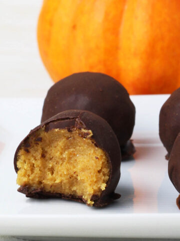 four chocolate covered pumpkin pie protein balls on a white plate with a bright orange mini pumpkin behind them