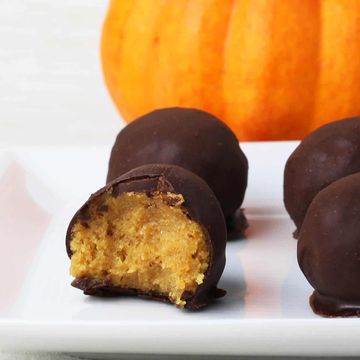 four chocolate covered pumpkin pie protein balls on a white plate with a bright orange mini pumpkin behind them