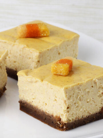 square cut pumpkin cheesecake bars with gingerbread crust and topped with protein candy corn on a white plate