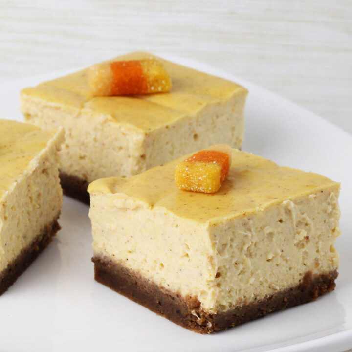 square cut pumpkin cheesecake bars with gingerbread crust and topped with protein candy corn on a white plate