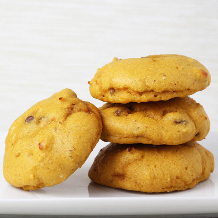 three stacked pumpkin protein cookies with a fourth cookie angled on the side of the stack, all on a white plate with a light background