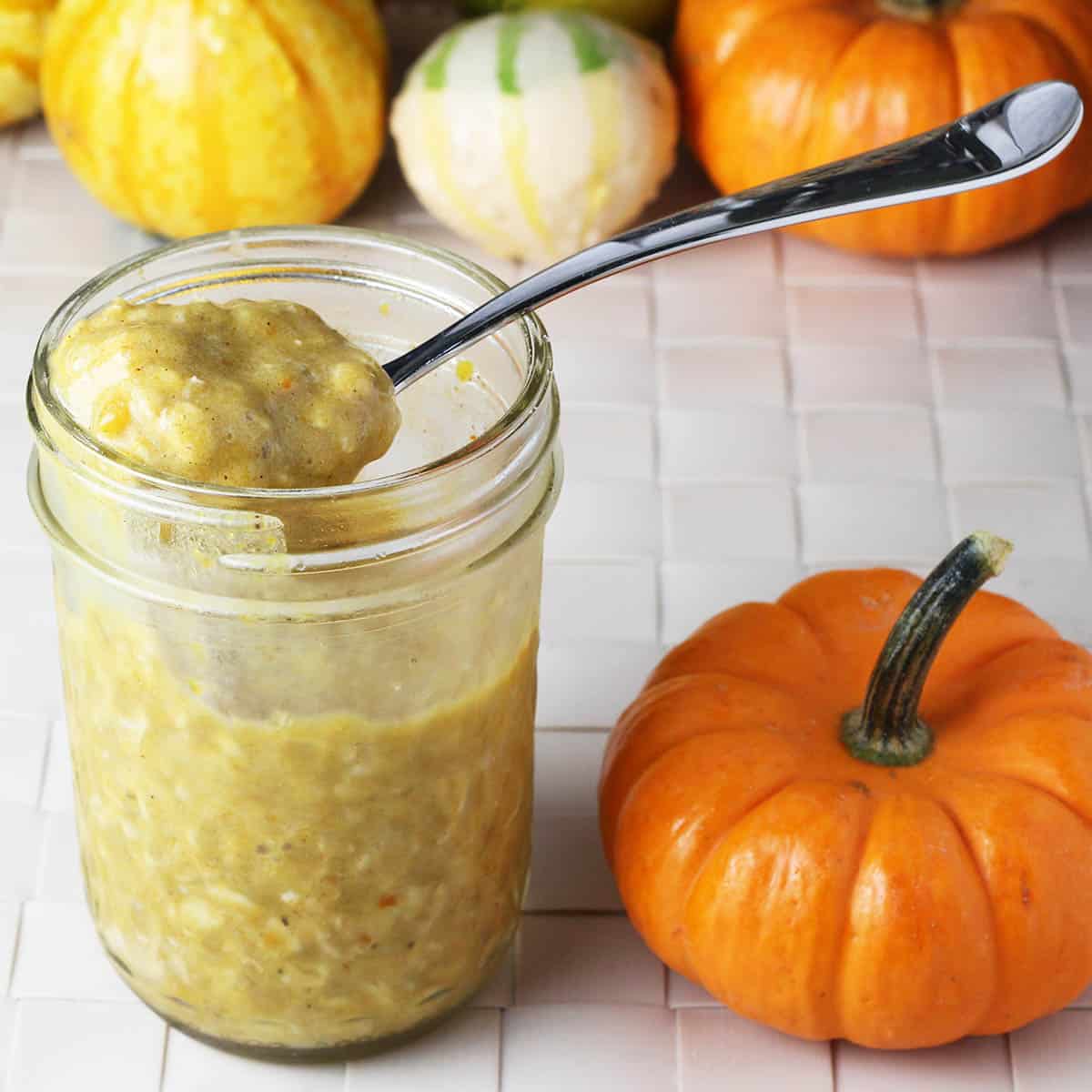 pumpkin spice overnight oats in a jar with a spoonful sitting on top and next to a mini pumpkin