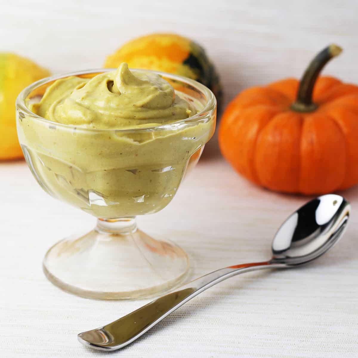 small dessert dish with pumpkin spice mousse with a small silver dessert spoon and a mini pumpkin in the background