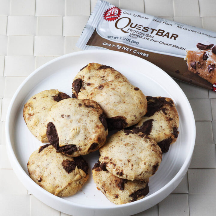 eight pieces of a chocolate chip cookie dough quest bar baked into cookies on a white plate and next to a packaged quest bar